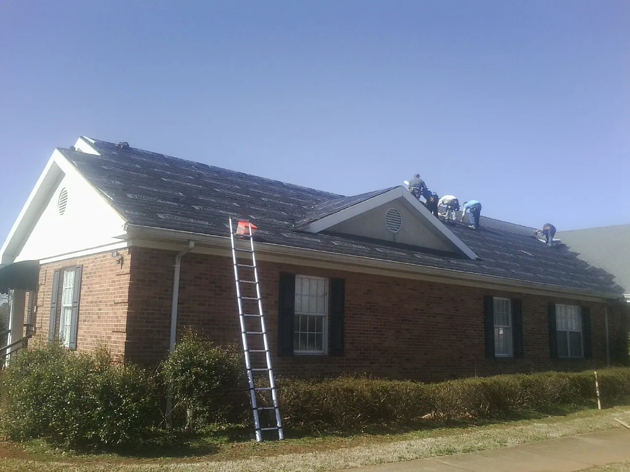 Crew tearing shingles off a brick ranch roof with a ladder set — Emergency Roof Repair work by our crew in Hartford