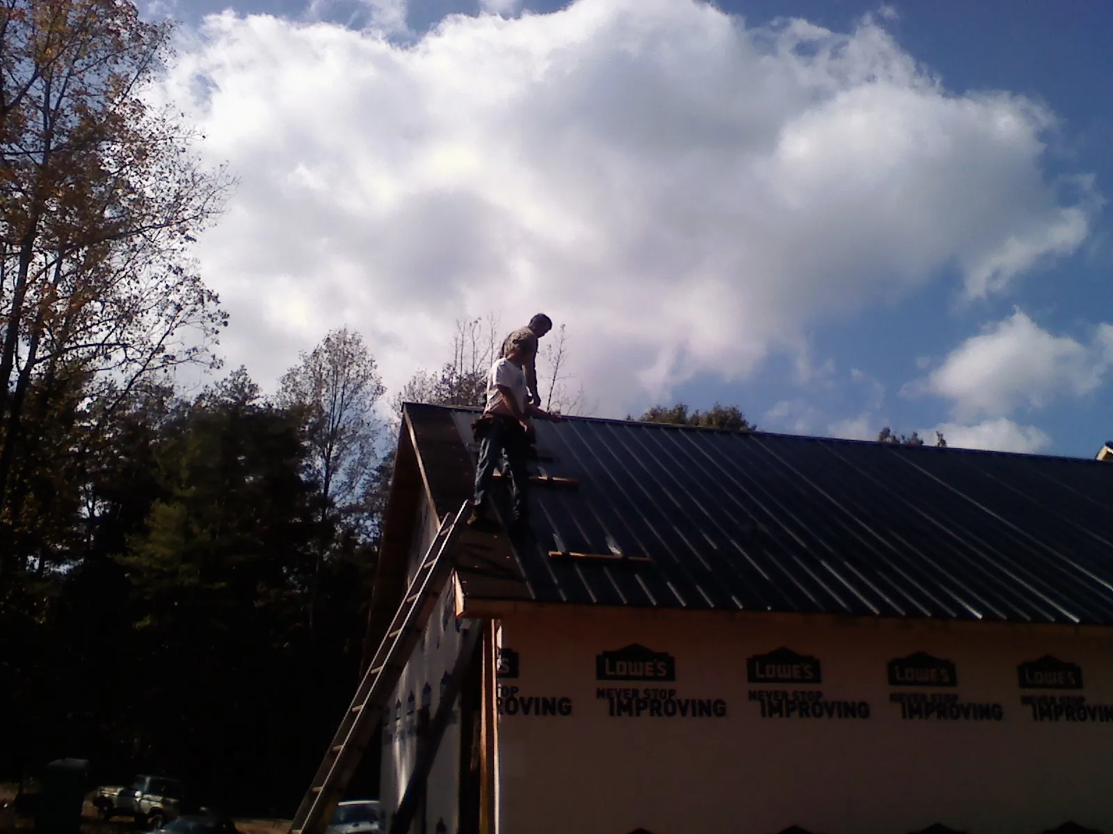 Roofer fastening dark metal panels high against a cloudy sky, from a Roof Inspection job in Hartford